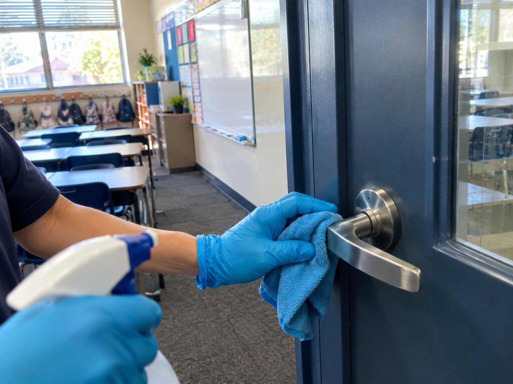 Gloved cleaner disinfecting a high-touch classroom door handle